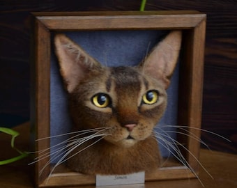 May include: A framed needle felted portrait of a brown Abyssinian cat with yellow eyes. The cat's name, "Simon", is written on a small tag below the portrait.
