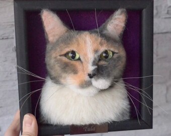 May include: A framed needle felted portrait of a calico cat with green eyes. The cat is looking directly at the viewer. The frame is black with a purple velvet mat. The name "Tula" is written on a small plaque below the cat.