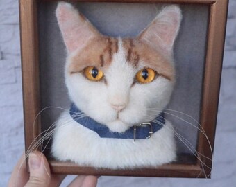 May include: A framed felted cat portrait. The cat has white fur with orange tabby markings, yellow eyes, and a blue denim collar. The portrait is set in a wooden frame.