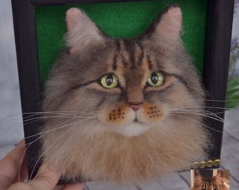 May include: A framed needle felted portrait of a long-haired cat with green eyes. The cat is brown and gray with a white chest. The frame is black with a green background.