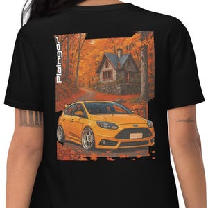 Könnte beinhalten: Schwarzes T-Shirt mit einer Grafik eines gelben Autos auf einer Straße, die zu einem Steinhäuschen führt, umgeben von Herbstlaub. Der Text "Plaingor" ist vertikal auf der linken Seite der Grafik aufgedruckt.