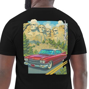 Könnte beinhalten: Schwarzes T-Shirt mit einer Grafik von Mount Rushmore und einem roten Oldtimer. Die Illustration enthält den Text "Plainges" in vertikaler Schrift. Das Auto fährt auf einer Straße mit grünen Bäumen und blauem Himmel.