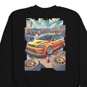 Peut inclure: Sweat-shirt noir avec une illustration vibrante d'une voiture de sport orange sur un circuit. L'image comprend une foule, une bannière et des roues de secours. La voiture est au centre, avec des phares et des jantes détaillés.