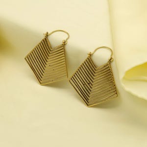 May include: A pair of gold-colored earrings. Each earring features a geometric, diamond-shaped design with layered horizontal lines. The earrings have a simple hook closure and are displayed on a light yellow fabric.