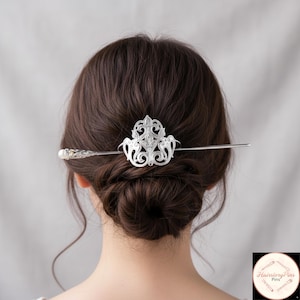 May include: A silver hair pin with an ornate, symmetrical design. The pin features a decorative centerpiece with a floral motif and a long, straight shaft. The hair accessory is worn in a bun, showcasing the intricate details of the hair jewelry.
