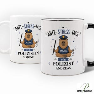 Könnte beinhalten: Zwei weiße Keramiktassen mit einem illustrierten Capybara in Polizeiuniform in Meditationshaltung. Das Design zeigt den Text ANTI-STRESS-TASSE FÜR POLIZISTIN SIMONE und ANTI-STRESS-TASSE FÜR POLIZIST ANDREAS sowie einen Schlagstock und Handschellen.
