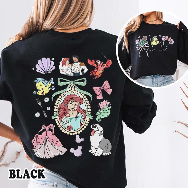 May include: Black sweatshirt featuring colorful illustrations of characters and elements from a popular animated film. The design includes a portrait of a princess, a seashell, a lobster, and other related graphics. The word "BLACK" is printed at the bottom.