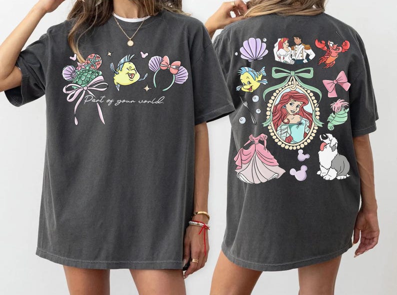 May include: Dark gray t-shirt featuring colorful illustrations from a popular animated film. The front displays a bow, a fish, and text that reads "Part of your world." The back has more characters and a portrait of a princess.
