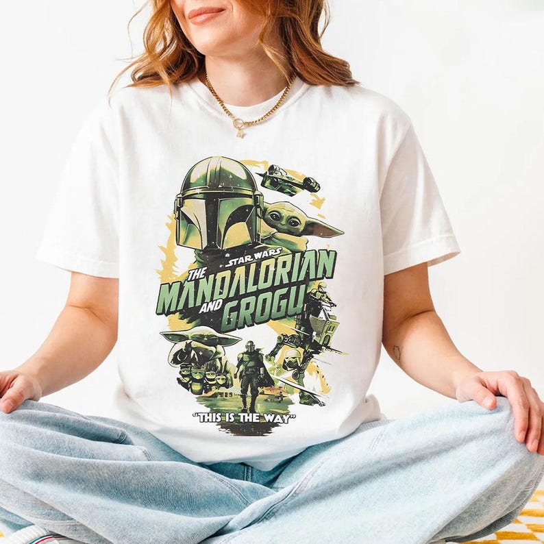 May include: White t-shirt with a Star Wars graphic featuring The Mandalorian and Grogu. The design includes the Mandalorian's helmet, Grogu, and the phrase "THIS IS THE WAY".