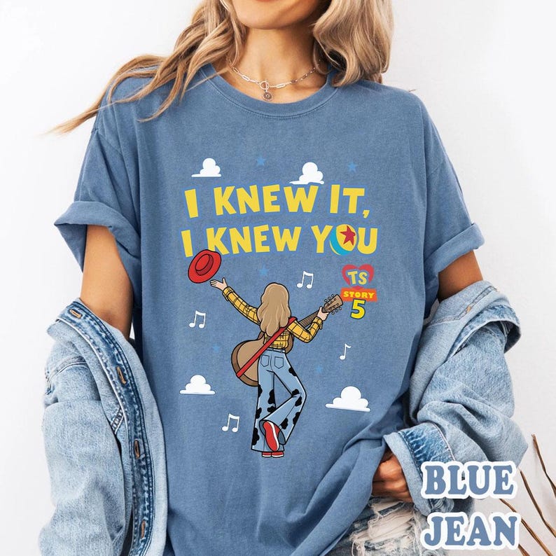 May include: A blue t-shirt featuring a graphic of a person with long hair playing a guitar, wearing a yellow plaid shirt and cow-print pants. The text reads I KNEW IT, I KNEW YOU, TS STORY 5, with clouds, music notes, a red hat, and a ball icon.