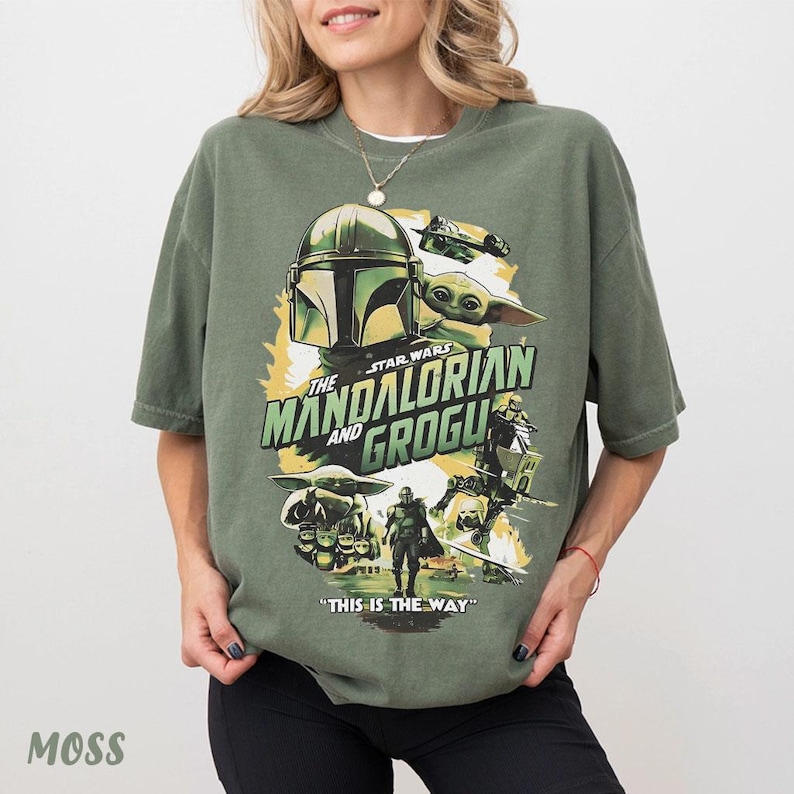 May include: Moss green t-shirt with a graphic design from The Mandalorian and Grogu. The design features the Mandalorian helmet, Grogu, and the text "The Mandalorian and Grogu" and "This is the Way".