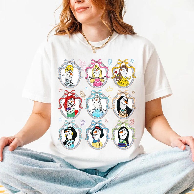 May include: White t-shirt featuring cartoon portraits of various characters in oval frames with bows. The characters include a snowman, a princess in a pink dress, and a princess in a yellow dress. The shirt is a casual wear item.