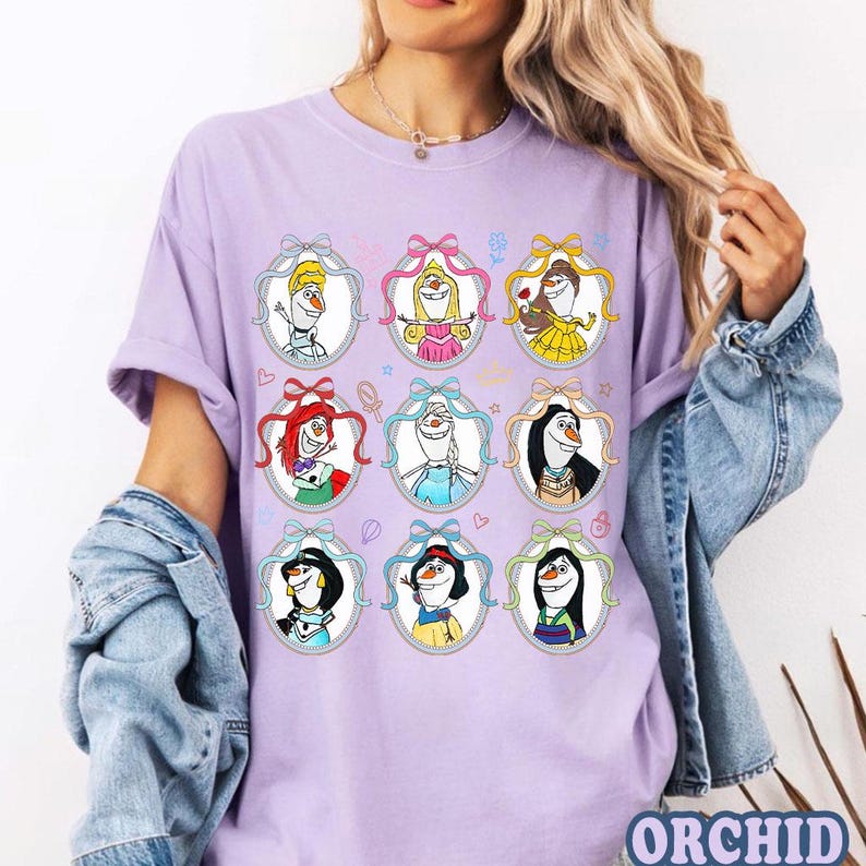May include: A light purple t-shirt featuring nine oval portraits of snowmen dressed as Disney princesses. Each portrait is framed with a decorative border and a bow. The shirt has short sleeves and a relaxed fit. The word "ORCHID" is printed at the bottom right.