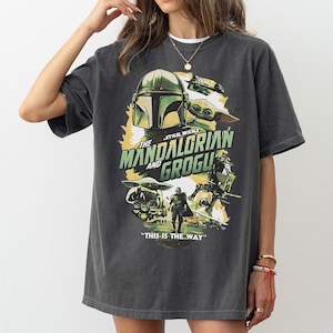 May include: Dark grey t-shirt with a graphic from the Star Wars series, "The Mandalorian and Grogu." The design includes the Mandalorian's helmet, Grogu, and the phrase "This is the Way."