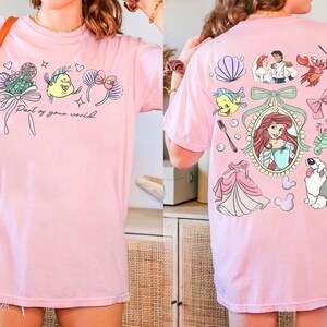 May include: Pink t-shirt featuring colorful cartoon graphics of characters and elements from a popular animated movie. The front of the shirt has the text "Part of your world". The back of the shirt has additional graphics.