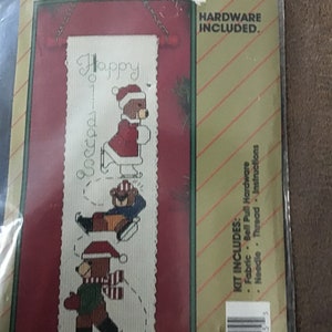 May include: A cross-stitch kit featuring three bears ice skating with the text "Happy Holidays" on a white background. The kit includes fabric, bell pull hardware, needle, thread, and instructions. The kit is packaged in a clear plastic bag with a red and gold background.