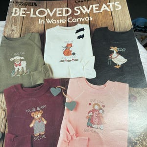 May include: A selection of embroidered sweatshirts in various colours, including green, white, burgundy, and pink. The designs feature a sheep, a cat, a goose, a teddy bear, and a family. Text includes "I LOVE EWE", "LOVE ME LOVE MY CAT", "YOU'RE BEARY SPECIAL", "GIVE LOVE GATHER LOVE".