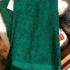 Puede incluir: Una toalla de color verde oscuro con un borde de flecos. La toalla est&aacute; doblada y tiene una etiqueta blanca con el texto "I Find".