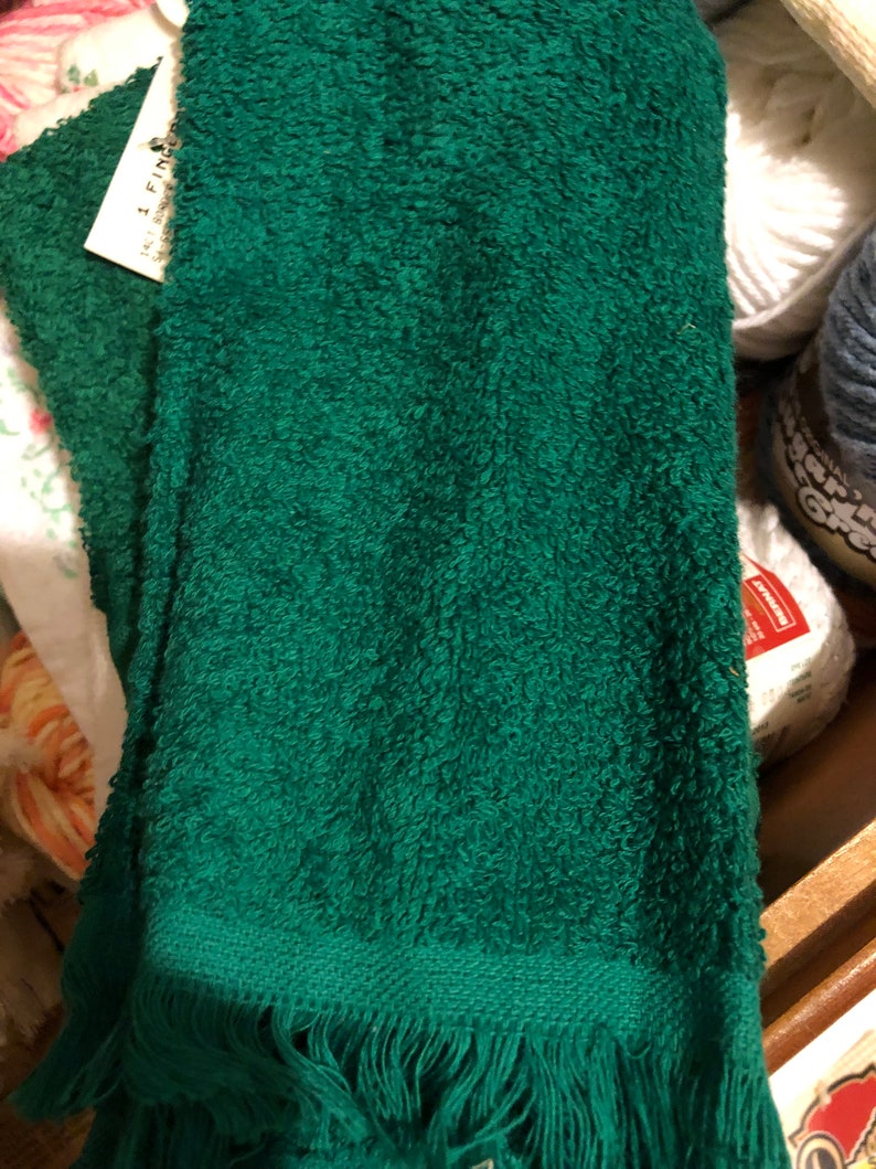 Puede incluir: Una toalla de color verde oscuro con un borde de flecos. La toalla est&aacute; doblada y tiene una etiqueta blanca con el texto "I Find".