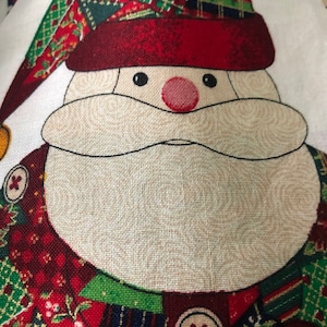May include: Close-up of a Santa Claus face made of fabric. The face is white with a red nose and black eyes. The Santa is wearing a red hat with a green and plaid pattern.