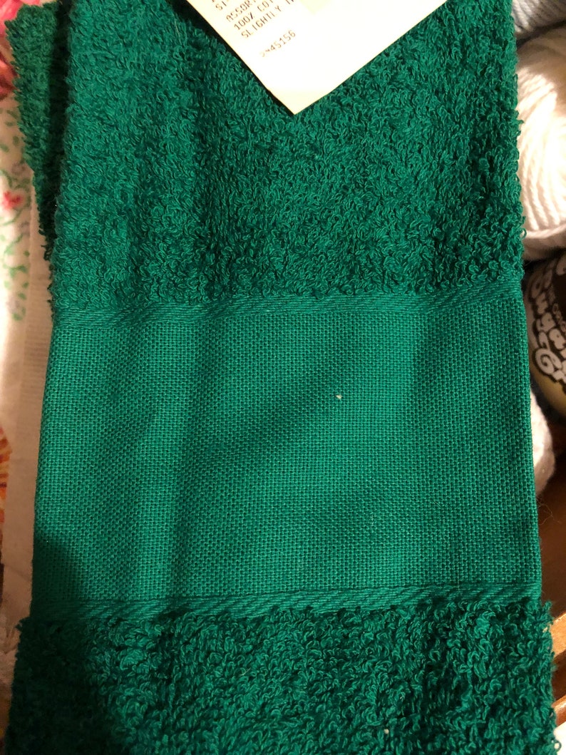 Puede incluir: Una toalla de mano verde con una superficie texturizada. La toalla tiene un borde tejido.