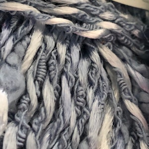 Op de afbeelding: Close-up van een bol garen in een lichtblauwe en witte kleurcombinatie. Het garen is zacht en pluizig, met een licht getextureerd uiterlijk.