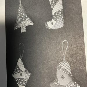 May include: Four handmade patchwork ornaments in the shape of a Christmas tree, stocking, diamond, and bell. Each ornament is made from different patterned fabrics and has a white star in the center.