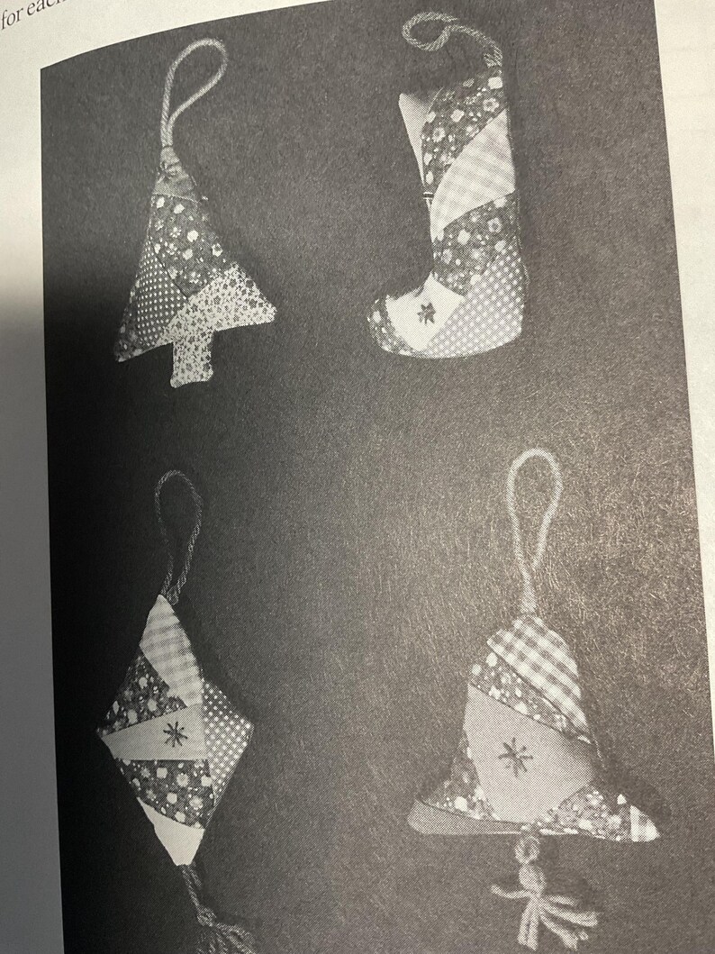 May include: Four handmade patchwork ornaments in the shape of a Christmas tree, stocking, diamond, and bell. Each ornament is made from different patterned fabrics and has a white star in the center.