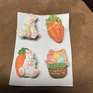 May include: Set of four Easter-themed ceramic buttons featuring a bunny holding an egg, a carrot, a bunny holding a carrot, and a basket of eggs.