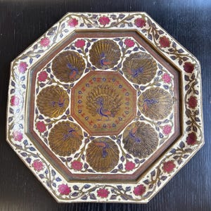 May include: An octagonal decorative tray with a detailed peacock design. The tray features a central peacock surrounded by seven additional peacocks. The tray has a cream-coloured border with red floral accents and a gold-coloured interior.
