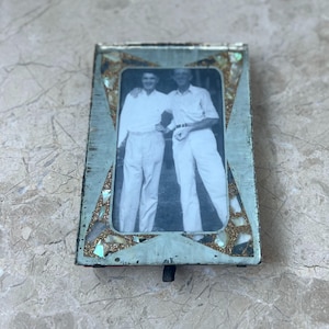 May include: Vintage rectangular photo frame with a black and white photograph of two men. The frame has a distressed teal finish with mosaic accents. A small, black stand is attached to the bottom.