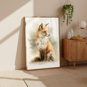 Op de afbeelding: Een ingelijste aquarelprint van een vos. De vos is afgebeeld in tinten oranje, wit en bruin, met een pluizige vacht en een alerte uitdrukking. Het kunstwerk is geplaatst tegen een zachte, vage achtergrond en ingelijst in licht hout.