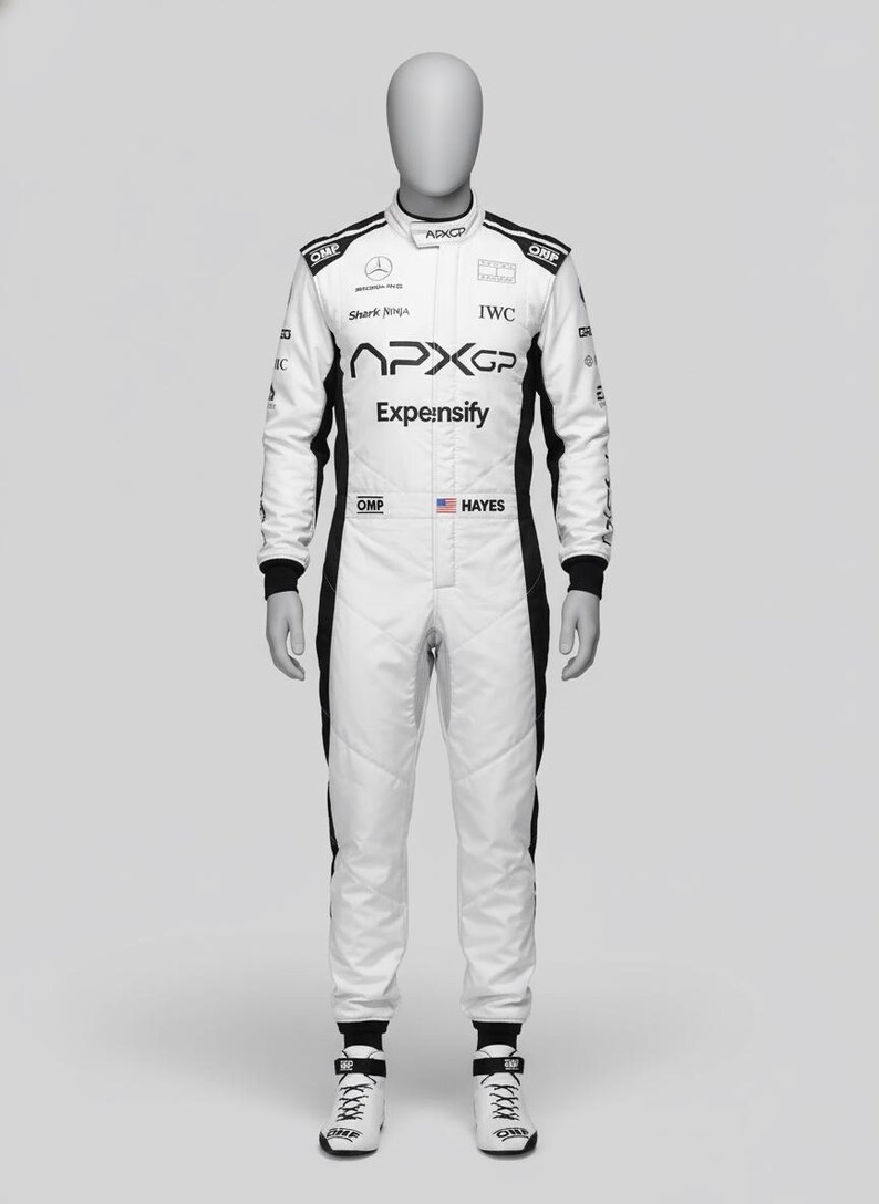May include: White racing suit with black accents, displayed on a mannequin. The suit features sponsor logos, including "APXGP" and "Expe:nsify." The name "Hayes" is printed on the chest. The suit is paired with white racing shoes.