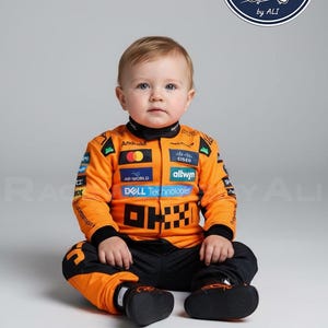 Könnte beinhalten: Ein Baby in einem orangefarbenen und schwarzen Rennanzug mit Sponsorenlogos wie "Android" und "Cisco". Der Anzug hat einen schwarzen Kragen und Manschetten. Das Baby sitzt und trägt schwarze Schuhe. Ein kreisförmiges Logo mit Rennflaggen befindet sich im Hintergrund.