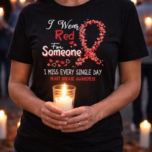 May include: Black t-shirt with the text "I Wear Red For Someone" and a red ribbon design. The shirt also includes the text "I miss every single day" and "Heart Disease Awareness". A lit candle is held in front of the shirt.