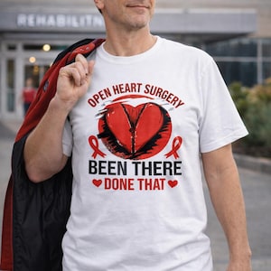 May include: White t-shirt with the text "OPEN HEART SURGERY BEEN THERE DONE THAT" in red and black. The design includes a red heart graphic and red ribbons. The shirt is worn by a person.