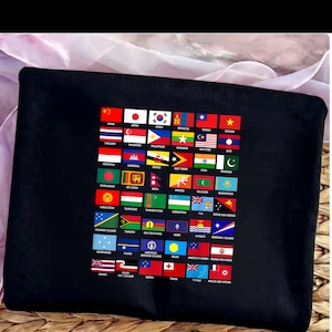 Può includere: Cuscino rettangolare nero con una stampa vivace di varie bandiere nazionali. Le bandiere sono disposte in un motivo a griglia, mostrando una vasta gamma di colori e design. Il cuscino è realizzato in un tessuto scuro e morbido.