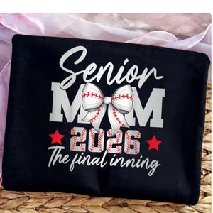 May include: Black baseball-themed accessory with the text "Senior Mom" in white script and block letters. A baseball-shaped bow is centered above the word "2026" and the phrase "The final inning". Two red stars flank the year.