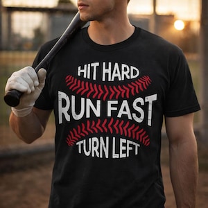 May include: Black t-shirt with the text "HIT HARD RUN FAST TURN LEFT" in white and red. The design incorporates a baseball theme, with the text arranged around a baseball graphic. The shirt is worn by a person holding a baseball bat.