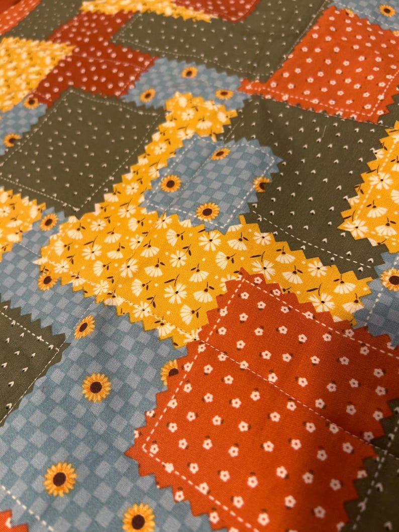 Pu&ograve; includere: Una trapunta patchwork con pezzi di tessuto rettangolari dai bordi dentellati. Il motivo include verde oliva a pois bianchi, arancione bruciato con fiori bianchi, quadretti vichy azzurri e giallo brillante con stampe floreali a margherita.