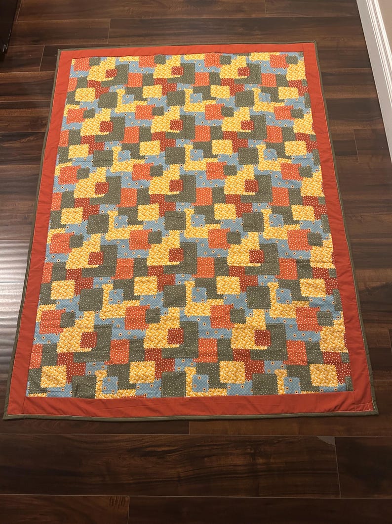 Pu&ograve; includere: Una trapunta rettangolare caratterizzata da un motivo geometrico di piccoli quadrati nei toni del giallo, arancione, azzurro e verde oliva. La trapunta &egrave; rifinita con un bordo arancione bruciato e un sottile profilo verde oliva.