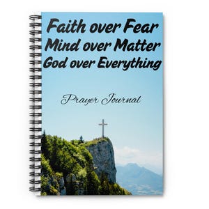 Puede incluir: Diario de oración con espiral con un fondo de cielo azul. La portada presenta el texto "Faith over Fear, Mind over Matter, God over Everything" y "Prayer Journal". Una cruz está en la cima de una montaña.