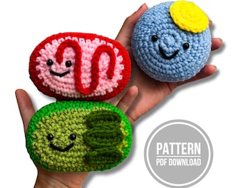 Op de afbeelding: Drie gehaakte knuffels met lachende gezichtjes en zwarte kraaloogjes. Eén is een lichtblauwe bol met een gele bovenkant, één een rood en roze ovaal met een rode kronkel, en één een groen ovaal met donkergroene accenten. Tekst: PATTERN PDF DOWNLOAD.