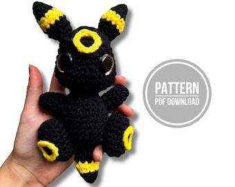 Op de afbeelding: Een zwart en geel gehaakt wezen met grote donkere ogen, puntige oren en cirkelvormige markeringen op het voorhoofd, de ledematen en de staart. Een cirkelvormige afbeelding rechts bevat de tekst PATTERN PDF DOWNLOAD in witte hoofdletters.