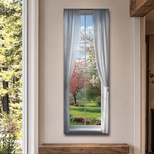 Puede incluir: Una obra de arte enmarcada que representa una vista de ventana de un vibrante jardín primaveral. La escena incluye un árbol de flores rosas, flores blancas, hierba verde y cielo azul. Cortinas transparentes enmarcan la ventana.