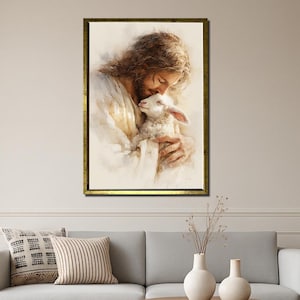May include: A framed watercolor painting depicts a figure with long brown hair embracing a lamb. The figure is wearing white robes, and the painting has a gold frame. The artwork is displayed above a gray sofa with decorative pillows.