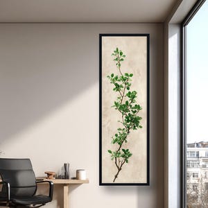 Op de afbeelding: Een ingelijste verticale kunstdruk met een botanische illustratie van een slanke tak met groene bladeren. Het kunstwerk is geplaatst tegen een beige achtergrond en ingesloten in een zwart frame, geschikt voor interieurdecoratie.