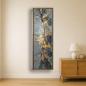 Könnte beinhalten: Vertikale Wandkunst mit einem strukturierten, abstrakten Design. Das Kunstwerk zeigt ein rissiges, steinartiges Aussehen in Grau- und Schwarztönen, akzentuiert mit Blattgold. Das Stück ist in einem goldfarbenen Rahmen eingefasst.