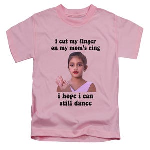 May include: A pale pink t-shirt featuring the text "i cut my finger on my mom's ring i hope i can still dance" above and below a photo of a young girl.
