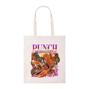 May include: White tote bag with a graphic of monkeys and the text "PUNCH the Monkey". The text is in purple and orange. The bag has two white handles and is made of a light-colored fabric.
